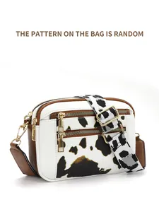 Detail view of cow print crossbody bag with multiple zippers and wide adjustable strap