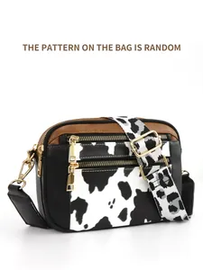 Detail showing cow print wide strap and multi-layer gold zippers on crossbody bag