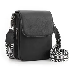 Dettaglio mini borsa a tracolla in pelle nera con ampia tracolla a righe regolabile