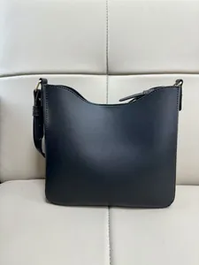 Close-up of black leather messenger bag with gold hardware on beige background