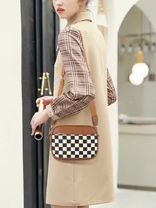 Detailed view of checkered crossbody camera bag with adjustable strap on female model