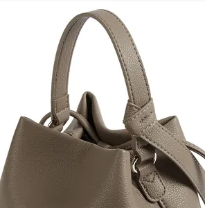 Detailed macro view of taupe bucket bag with litchi grain leather and drawstring closure