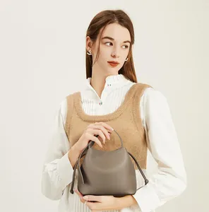 Detail view of a grey grained leather bucket bag with drawstring and top handle on a model