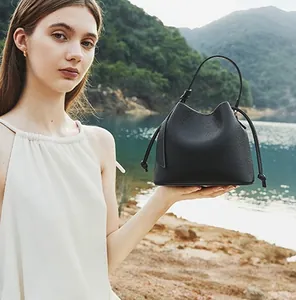 Elegant black pebbled leather bucket bag shown by a model against a scenic lake backdrop