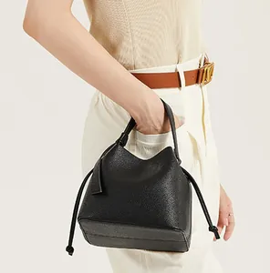 Detail of black lychee grain leather bucket bag with drawstring and top handle on model