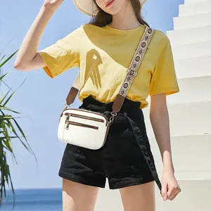 White crossbody bag with brown trim and floral print wide strap on beach background