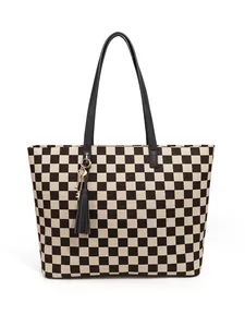 Gros plan du sac cabas à damier montrant la texture toile, anses cuir et breloque dorée