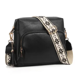 Black leather crossbody bag with patterned strap and fringe tassel on white background