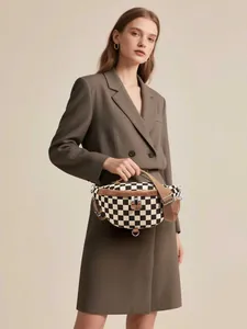 Detail of checkered canvas chest bag with brown leather trim and metal zipper accents