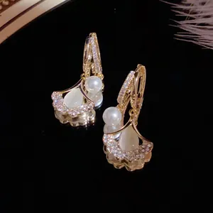 Detailed view of golden ginkgo leaf earrings with shimmering crystals and white pearls