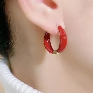 Close-up of a model wearing the C-shaped red enamel hoop earring with golden metallic edges