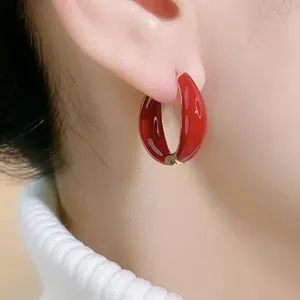 Red enamel C-shaped hoop earrings with gold metal edges worn on a white sweater