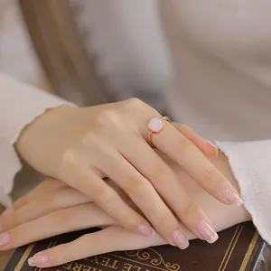 Elegante anello in oro rosa con pietra di giada bianca quadrata indossato da una modella