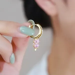 Dettaglio di orecchini a cerchio dorati con zirconi rosa e accenti floreali pendenti