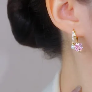 Dettaglio di orecchini a fiore con zircone rosa, perla e cerchietto dorato