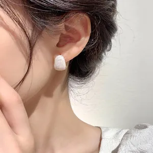Close-up of a white matte geometric stud earring with gold plating on a model ear