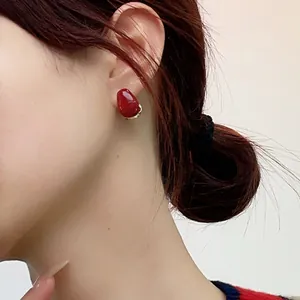 Macro shot of red enamel oval earrings with gold-plated base worn on model's ear