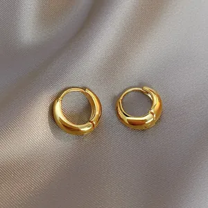 Dettaglio ravvicinato di orecchini a cerchio dorati su elegante sfondo di seta champagne