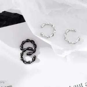 Détail des boucles d'oreilles à clip torsadées argentées et noires sur fond texturé