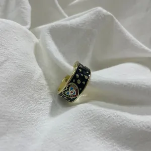 Dettaglio di anello placcato oro con smalto nero e motivi a cuore con occhio magico