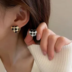 Elegant checkerboard heart earrings with black enamel and zircon inlay worn on ear