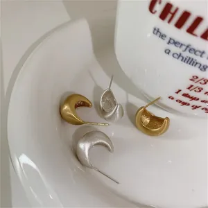 Detailed view of matte gold and silver crescent stud earrings on a ceramic tray