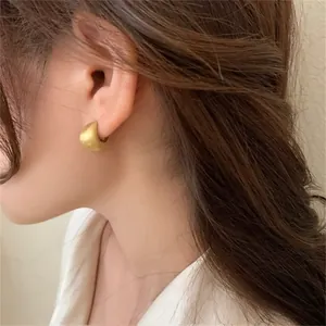 Close-up of model wearing matte gold C-shaped earrings with brushed vintage texture