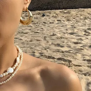 Orecchini a cerchio dorati lucidi e collana di perle a strati indossati da una modella