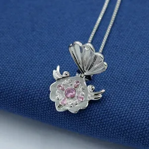 Detail of opening silver shell pendant with pink crystals and intricate floral filigree