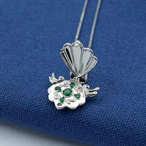 Silver shell-shaped necklace with green crystals on a deep blue textured fabric background