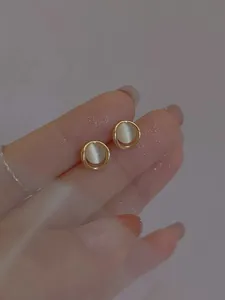 Nahaufnahme von runden Goldohrringen mit Opal in den Fingern gehalten im minimalistischen Stil