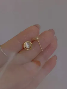 Detailansicht runder Opal-Ohrstecker mit Goldfinish zur Größenbestimmung am Finger gehalten