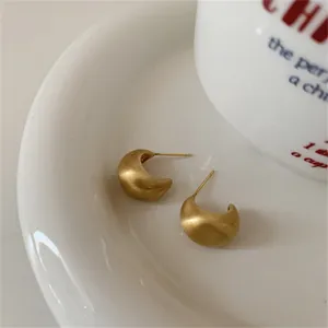 Matte gold crescent stud earrings with a brushed finish on a white ceramic tray