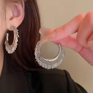 Dettaglio degli orecchini a cerchio argento con nappe metalliche pendenti sul modello