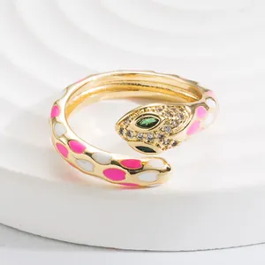 Macro detail of gold snake ring with pink enamel dots and green gemstone eyes