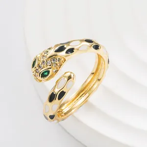 Adjustable snake ring in gold finish with black and white enamel dots and green eyes