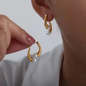 Detailed close-up of gold curved earrings with two white pearls on female model