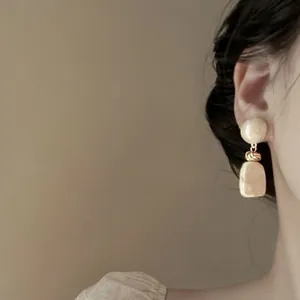 Dettaglio di eleganti orecchini pendenti in resina crema con maglie dorate su modella femminile