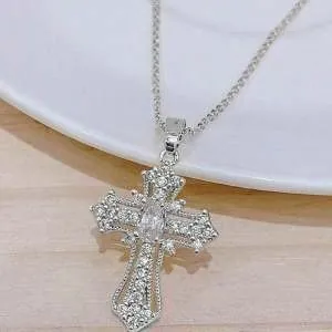 Macro view of silver cross pendant necklace with ornate stones on white ceramic plate