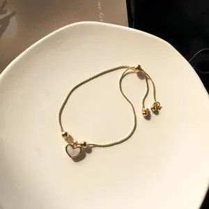 Detail of adjustable gold heart bracelet featuring white inlay in a white ceramic dish