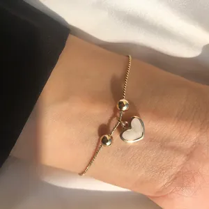 Detail of gold heart charm bracelet with white shell inlay on female model wrist