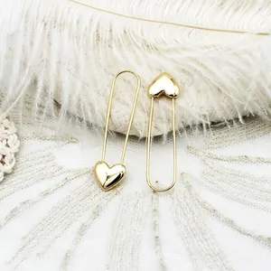 Elegant gold safety pin earrings with 3D heart design on a minimalist feather background
