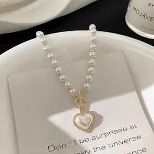 Close-up of pearl necklace featuring golden T-bar toggle clasp and a sparkling heart pendant