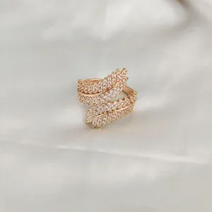 Detailed view of a gold feather ring with sparkling white cubic zirconia on white silk