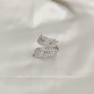 Macro detail of silver double feather open ring with zircon pavé on white silk fabric