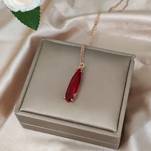 Elegant 16K gold teardrop red gemstone necklace on champagne silk gift background