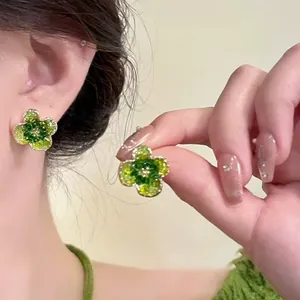 Detail of green crystal floral stud earrings shown on model with gold-tone accents