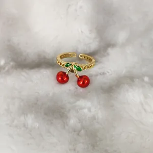 Detailaufnahme eines goldfarbenen Kirschrings mit roter Emaille auf weißem Plüschstoff