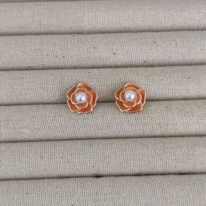 Elegant orange camellia stud earrings with gold edges and pearl center on display