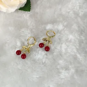 Elegante goldene Kirschohrringe mit roten Perlen auf weichem weißem Hintergrund
